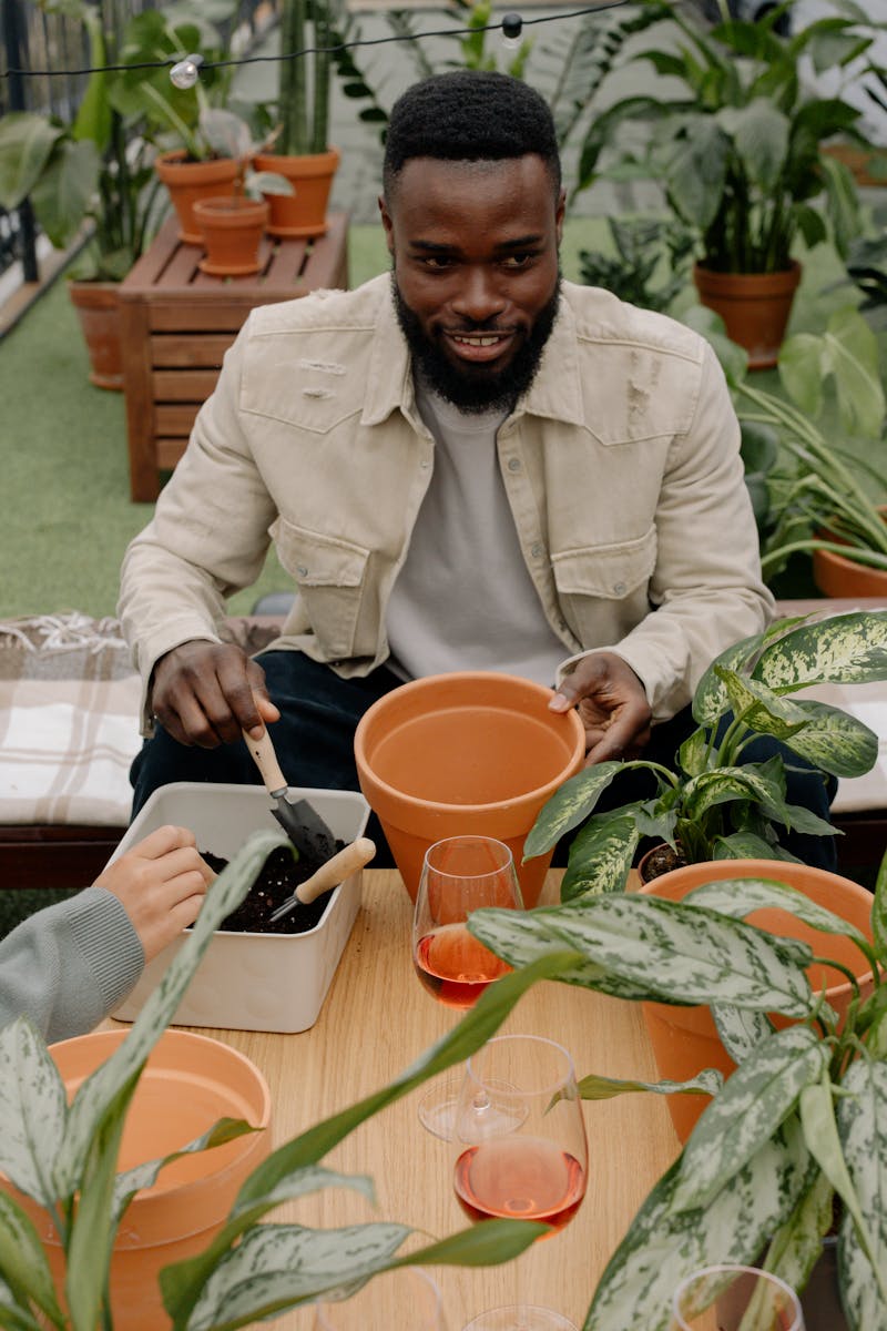 Man enjoying indoor gardening with clay pots and plants on a wooden table.